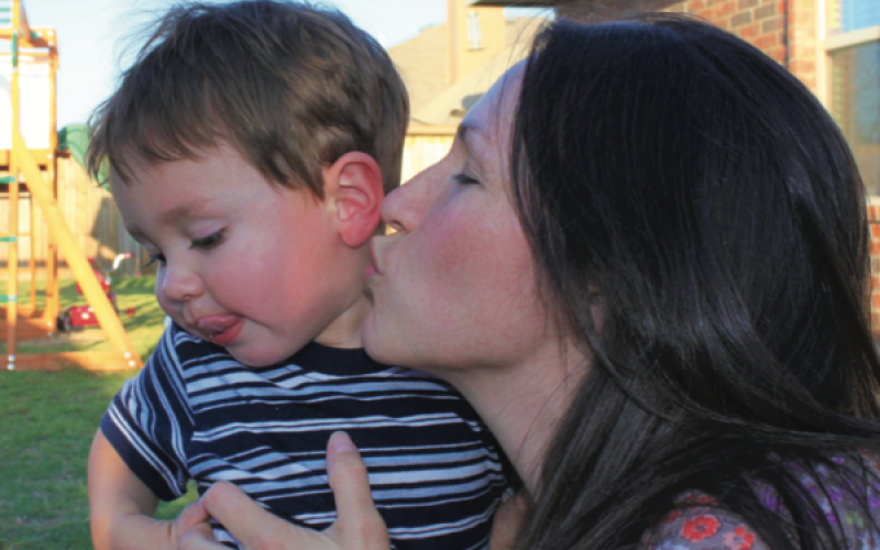 A mom cuddles up close to steal a kiss from her toddler.