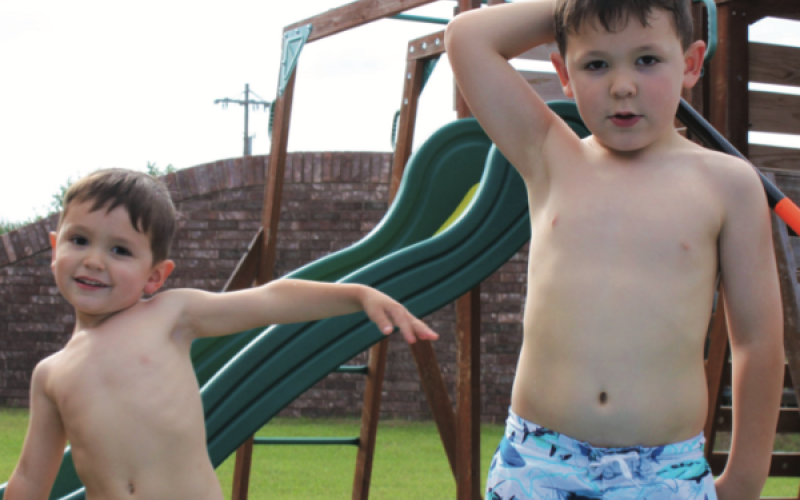 Two brothers enjoy a sunny day getting wet in their swimsuits.