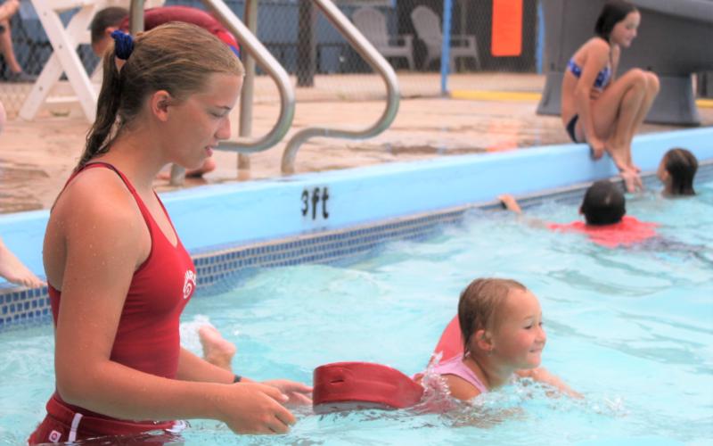 Rachel Gregg, high school lifeguard, watches as Brynlee Sanders of Cyril, age 4, uses a flotation device to swim the width of the pool.