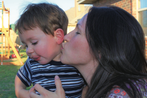 A mom cuddles up close to steal a kiss from her toddler.