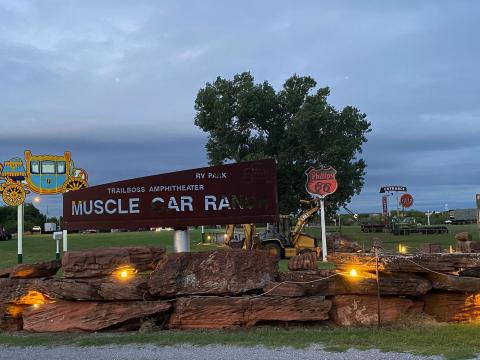 Muscle Car Ranch owner Curtis Hart and Ranch Hand Randy work to install a Phillips 66 sign just before dusk Wednesday evening. The orange and black sign replaces a red and white Phillips 66 sign that was dislodged during a 2013 tornado that hit Chickasha, Hart said. The replacement sign came down as hurricane Camile made landfall in Corpus Christi in 1969. Featuring chart-topping artists and bands from several genres, Hart’s Muscle Car Ranch has held concerts since 1992. Photo by Curtis Awbrey